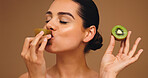 Beauty, kiwi and eating with woman in studio for vitamin c, nutrition and antioxidants glow. Self care, healthy food and natural enzyme with person and fruit on brown background for diet and detox