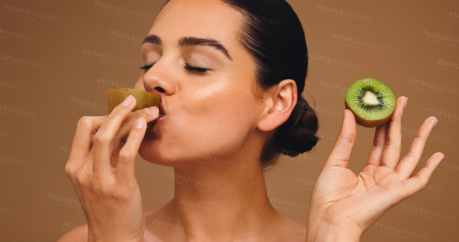 Buy stock photo Beauty, kiwi and eating with woman in studio for vitamin c, nutrition and antioxidants glow. Self care, healthy food and natural enzyme with person and fruit on brown background for diet and detox