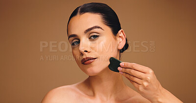 Buy stock photo Cosmetics, skincare or woman with gua sha in studio, self care or facial practice for radiant face. Portrait, space or person with beauty tool, reduce inflammation or skin routine on brown background