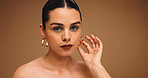 Earrings, beauty and woman with makeup for aesthetic, glow and shine on brown background. Ear jewelry, portrait and model with lipstick cosmetics, face transformation and confidence in studio
