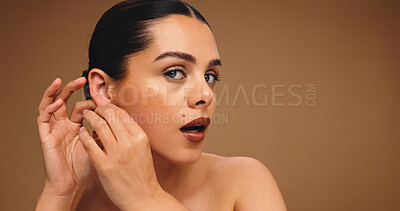 Buy stock photo Makeup, earrings and woman in studio for aesthetic, glow and shine on brown background space. Beauty, ear jewelry and model with lipstick cosmetics, face transformation and portrait with change