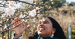 Outdoor, woman and touching branch in nature with flower, gratitude and laughter on university vacation break. Wellness, female person and spring season in park with zen, calm and peace in garden. 