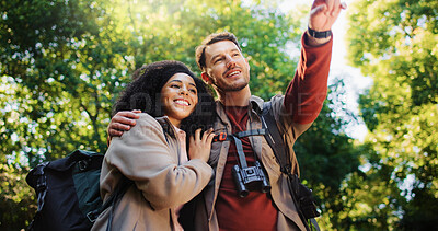 Buy stock photo Happy couple, hiking and point in woods for direction with search, break and hug with love for tourism. Man, woman and interracial relationship with sightseeing, smile or trekking adventure in forest