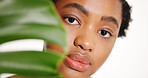 Portrait, skincare and black woman with leaf in studio for natural beauty, glow or organic cosmetics. Face, aesthetic and model with monstera plant, eco friendly dermatology and white background