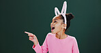 Happy girl, pointing and studio with bunny ears for advertising or marketing on a green background. Child, kid or showing space with wow, surprise or shock for amazing deal or notification on mockup