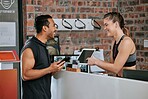 Asian man joining gym on digital tablet as member with caucasian trainer. Young coach helping, pointing and showing plan on technology. Two active fit people standing together in healthy fitness club