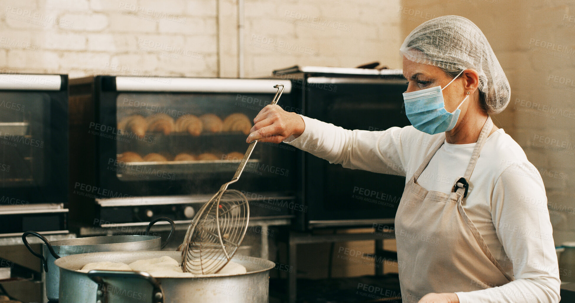 Buy stock photo Mask, baker or frying donuts in kitchen for dessert production, baking process or catering. Hospitality industry, mature person and lunch snack preparation in bakery for gastronomy or culinary safety
