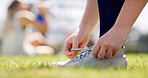Person, hands and tying shoes with preparation on grass field for sport, game or outdoor match. Closeup, athlete or player getting ready with sneaker, tie or laces for warm up, exercise or training