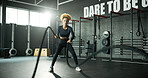 Woman, battle rope and workout in gym for cardio, exercise and body building for fitness. Intense routine, muscle and wellness with power for strength training, weight equipment and bicep challenge