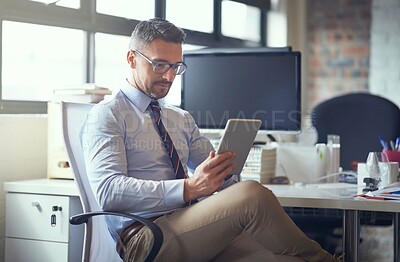 Buy stock photo Cropped shot of a businessman using his digital tablet while sitting in his office
