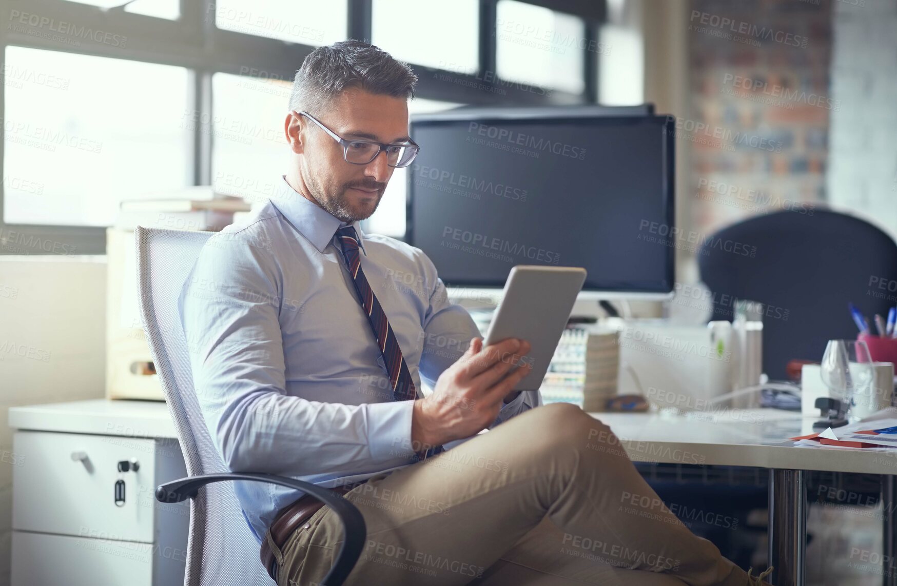 Buy stock photo Cropped shot of a businessman using his digital tablet while sitting in his office