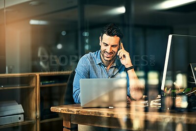 Buy stock photo Shot of a young businessman talking on his phone and using a laptop during a late night at work