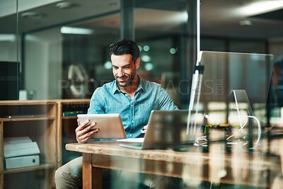 Buy stock photo Shot of a young businessman using a digital tablet at his desk in a modern office