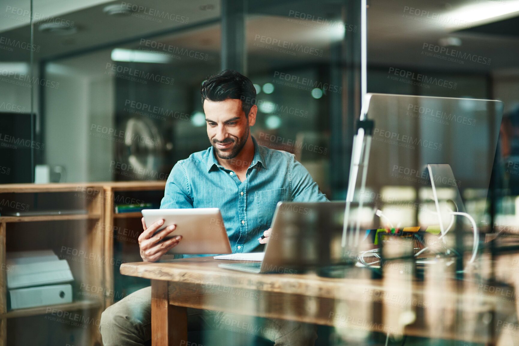 Buy stock photo Shot of a young businessman using a digital tablet at his desk in a modern office