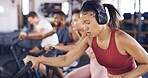 Headphones, gym and woman on stationary bike for exercise, training and cardio workout for health. Sports club, sweat and people on machine for cycling, wellness or fitness with music, radio or audio