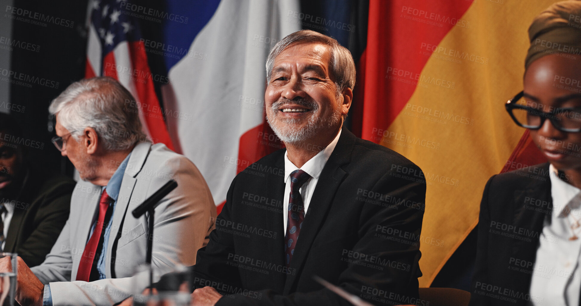 Buy stock photo Man, flags and portrait on panel at conference, happy and pride with international delegation for peace. Mature person, politician and global leader with group, smile or negotiation for war ceasefire