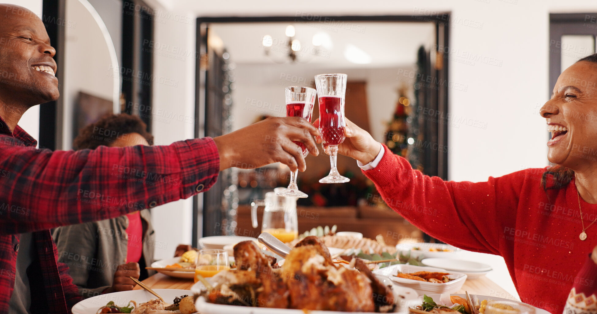 Buy stock photo Christmas, food and parents with drinks cheers in home for celebration, festive feast and bonding. Lunch, excited african family and meal toast at dinner table for holiday tradition or xmas gathering