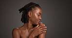 Black woman, relax and studio with skincare for beauty or cosmetics on a gray background. Calm, female person or model with smile, shoulder or touch for dermatology, hygiene or shine on mockup space