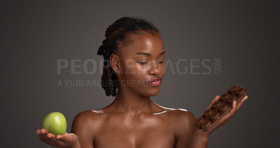 Buy stock photo Apple, chocolate and choice with black woman in studio for options or selection of food snack. Decision, fruit and slab with African model on gray background or mockup space for diet and wellness
