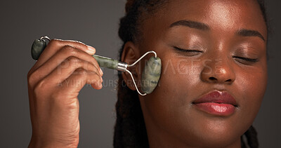 Buy stock photo Black woman, beauty and skincare with jade roller in studio for facial massage on a gray background. Female person, model or relaxation with spa tool for collagen, blood circulation or dermatology