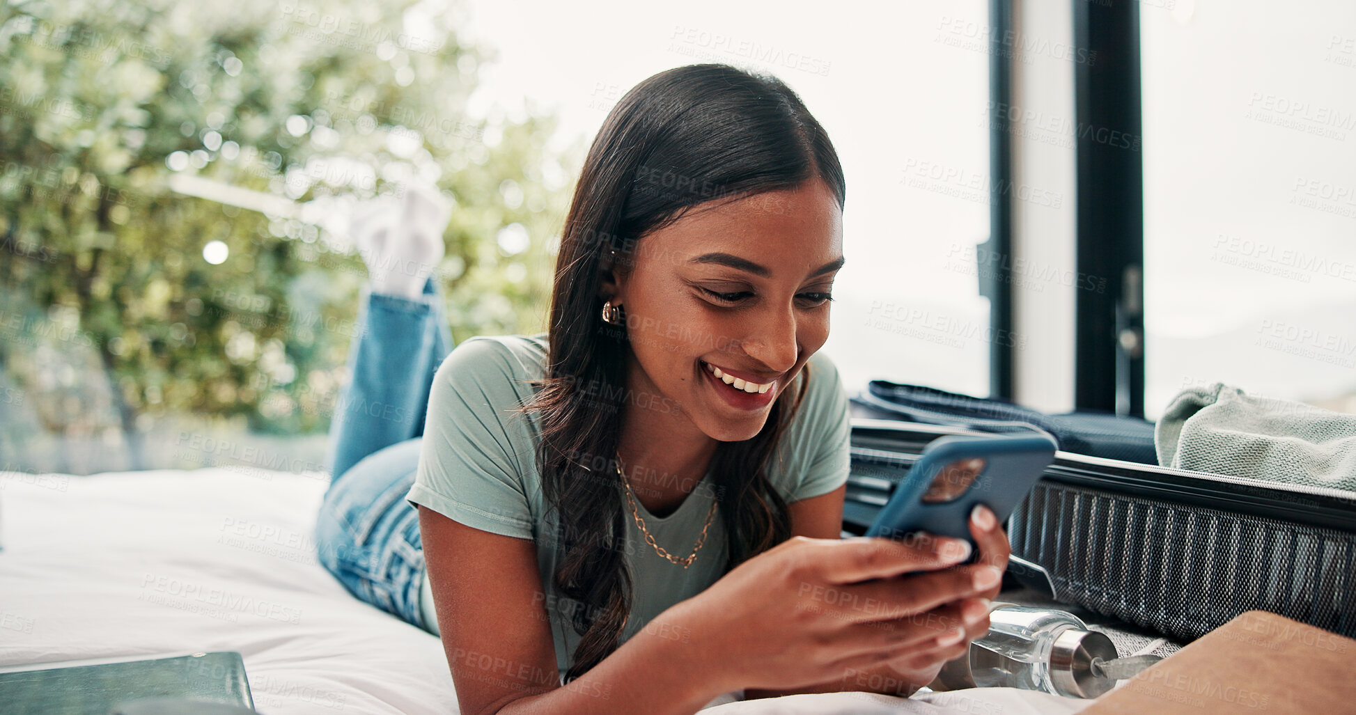 Buy stock photo Happy woman, travel and unpacking with phone in bed for vacation, holiday or accomodation in hotel. Female person, traveler or tourist with smile, mobile smartphone or suitcase for check in app
