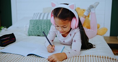 Buy stock photo Headphones, child and writing in notebook on bed, streaming music or homework activity for learning. Audio tech, education or girl in home for knowledge development, school task or listening to radio