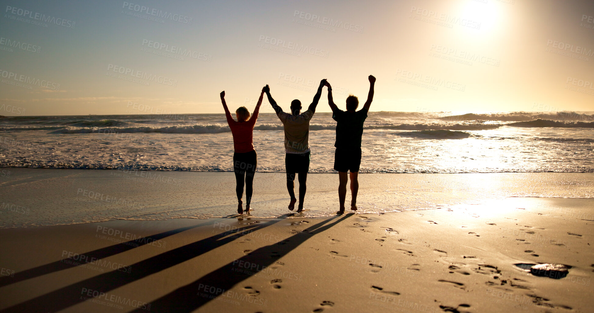 Buy stock photo Arms up, silhouette and people at beach with sunset, connection or celebration in trip success. Back, holding hands or friends at ocean with flare, adventure or travel achievement in summer evening.