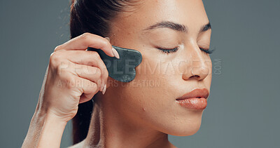 Buy stock photo Beauty, woman or gua sha in studio with massage for skincare, dermatology and facial tension. Relax, female person or cosmetic tool for lymphatic drainage, wellness or smooth skin on gray background.