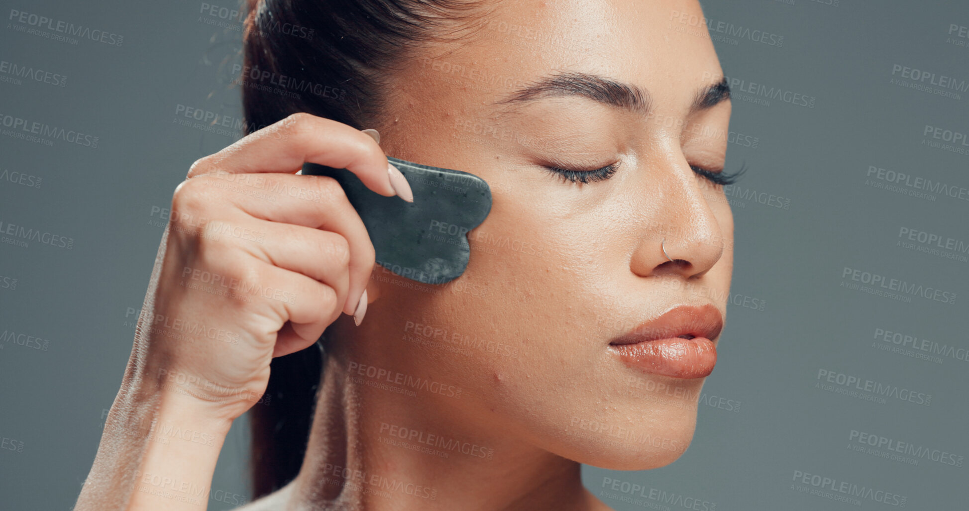 Buy stock photo Beauty, woman or gua sha in studio with massage for skincare, dermatology and facial tension. Relax, female person or cosmetic tool for lymphatic drainage, wellness or smooth skin on gray background.