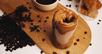 Buy stock photo Splash, coffee and beans with glass on table in kitchen of home for caffeine beverage, breakfast and morning brew. Cappuccino, iced latte drink and prepare with above of cup in apartment for liquid