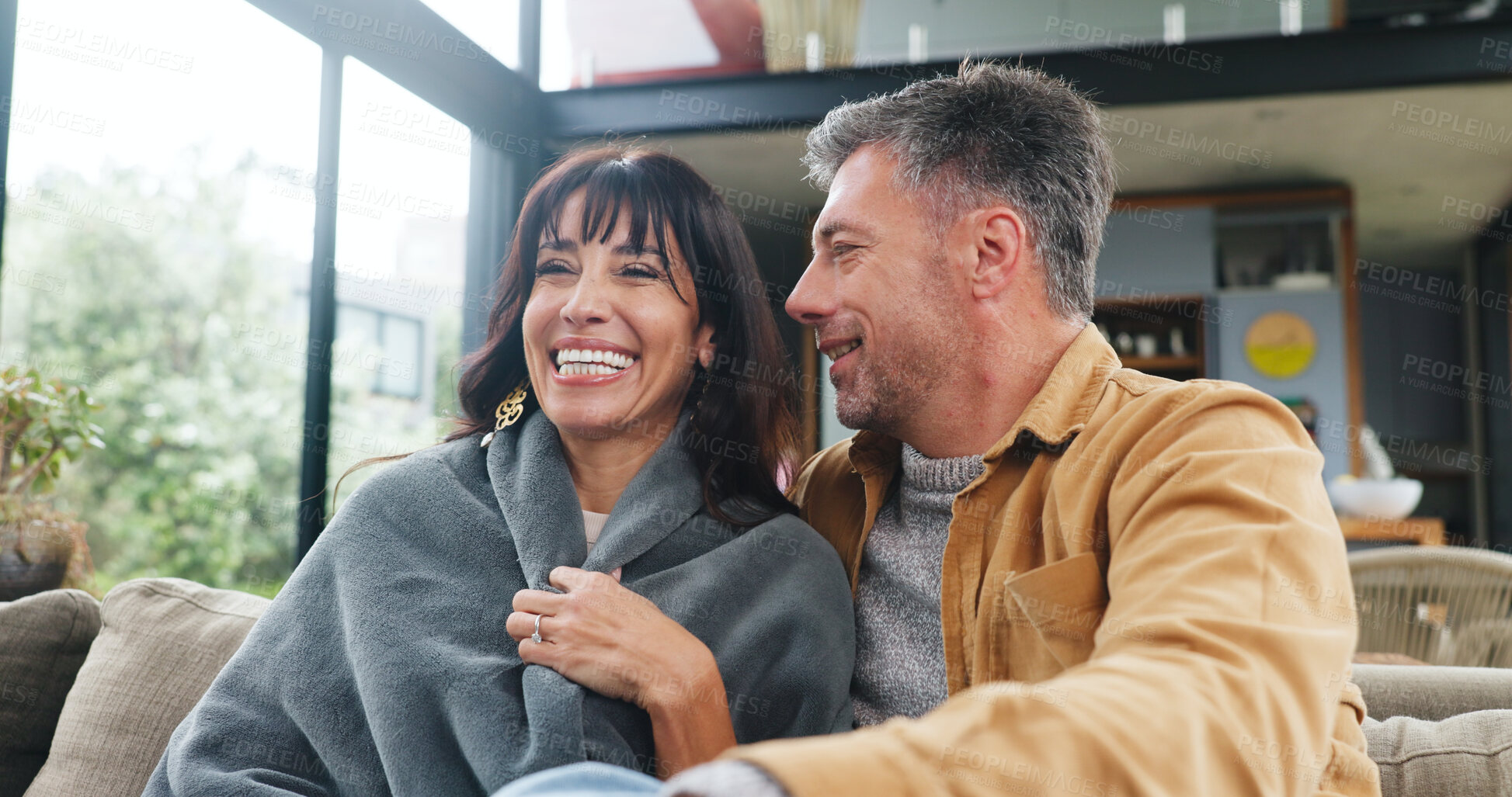 Buy stock photo Love, couple and relax with laughing on sofa for cozy weekend, funny conversation or connection. Happy, mature people and comfortable with blanket in home for holiday break, bonding together and joke