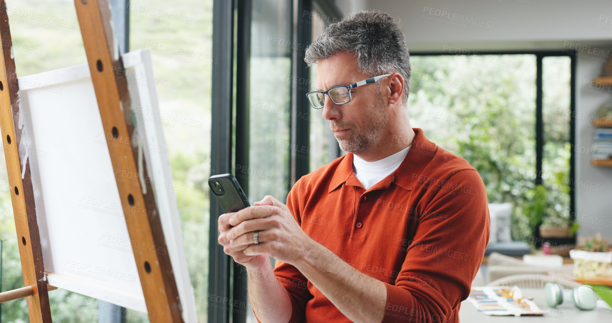 Buy stock photo Painting, phone and search with man in home for design reference, artist project and contact. Creative inspiration, artwork and canvas with mature person  and tech in apartment studio for hobby