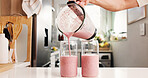 Hand, pour smoothie and glasses in kitchen with blender, organic nutrition and antioxidant benefits. Person, strawberry and protein shake in home with jug for digestive health, hydration or beverage.