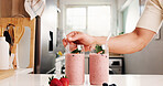 Hand, smoothie and glasses in kitchen with fruit drink, organic nutrition and antioxidant benefits. Person, strawberry and protein shake in home for digestive health, morning beverage and hydration.