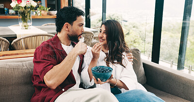 Buy stock photo Blueberries, eating and relax with couple on sofa in living room of home together for bonding. Bowl, healthy snack and hunger with happy people in apartment for love, organic diet or nutrition