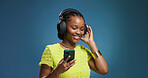 Headphones, cellphone and black woman in studio with music, radio or song for rhythm and energy. Happy, audio tech and African person listening to album on phone with mobile app by blue background.