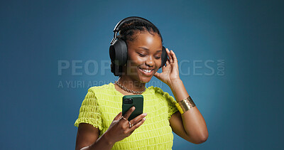 Buy stock photo Headphones, cellphone and black woman in studio with music, radio or song for rhythm and energy. Happy, audio tech and African person listening to album on phone with mobile app by blue background.