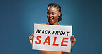 Happy, black woman and portrait with sale sign for Friday discount on a blue studio background. Female person, promoter or model with poster or billboard for offer, advertising or marketing deal