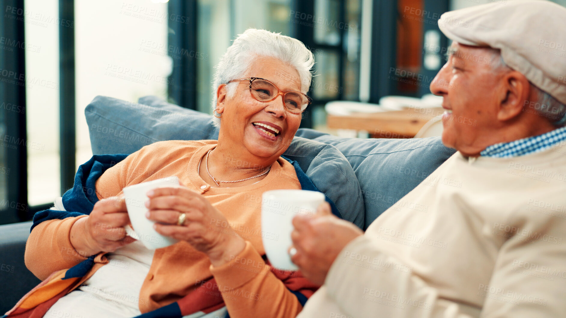 Buy stock photo Tea, senior couple and relax on sofa with funny conversation, retirement support and bonding. Love, elderly people and laughing with beverage in home for weekend break, healthy relationship and trust