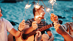 People, hands and night with fireworks on beach for new year, outdoor event or social gathering. Group, friends or sparklers with celebration in late evening for holiday or weekend on ocean coast