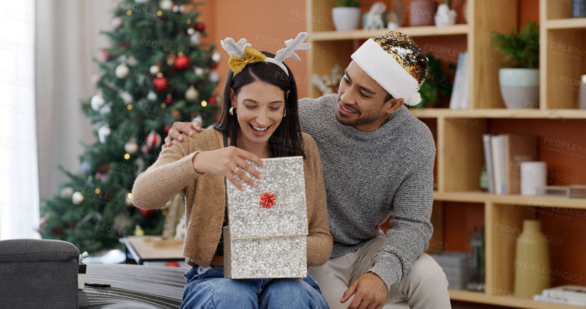 Buy stock photo Christmas, couple and smile in living room with gift for holiday tradition, connection or gratitude. Married people, present and embrace in house for festive season, appreciation or bonding together.