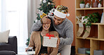 Christmas, home and couple with gift, surprise and bonding together with happiness, wow and tradition. Xmas, apartment or man with woman, shocked and celebration with present or festive season