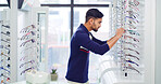 Eye care, man and shopping for glasses, vision and eyesight improvement with choice at shelf. Store, eyewear and person with frame for optometry, check spectacles and customer with lens for health