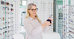 Vision, woman and cleaning glasses in shop, eye care and maintenance of stock with smile. Store, wipe eyewear and mature person with cloth fabric for frame, optometrist and spectacles for health