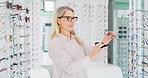 Vision, woman and cleaning glasses in store, eye care and maintenance of stock with smile. Shop, eyewear and mature person with cloth fabric for frame, optometrist and check spectacles for health