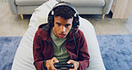 Beanbag, esport and man playing video game with controller in living room for virtual challenge in home. Gamer, headphones and male person for online streaming, entertainment or competition in lounge