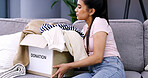 Woman, box and donation with clothing on sofa for charity, community service or welfare in home. Female person, package or parcel with garment collection for giveaway, change or volunteer in house