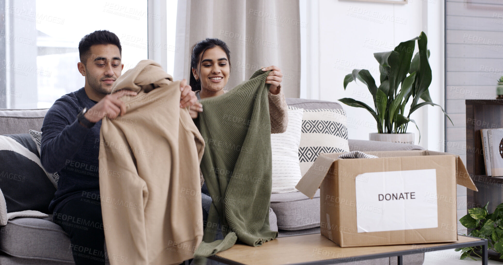 Buy stock photo Couple, folding clothes and donation box on sofa for charity initiative, nonprofit or declutter home. Married people, apparel giveaway and package in house for NGO support, parcel or spring cleaning.