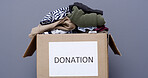 Clothes, charity and donation box in studio for non profit, humanitarian aid or support package. Cardboard, garments and community care with outreach, ngo or help for philanthropy on gray background