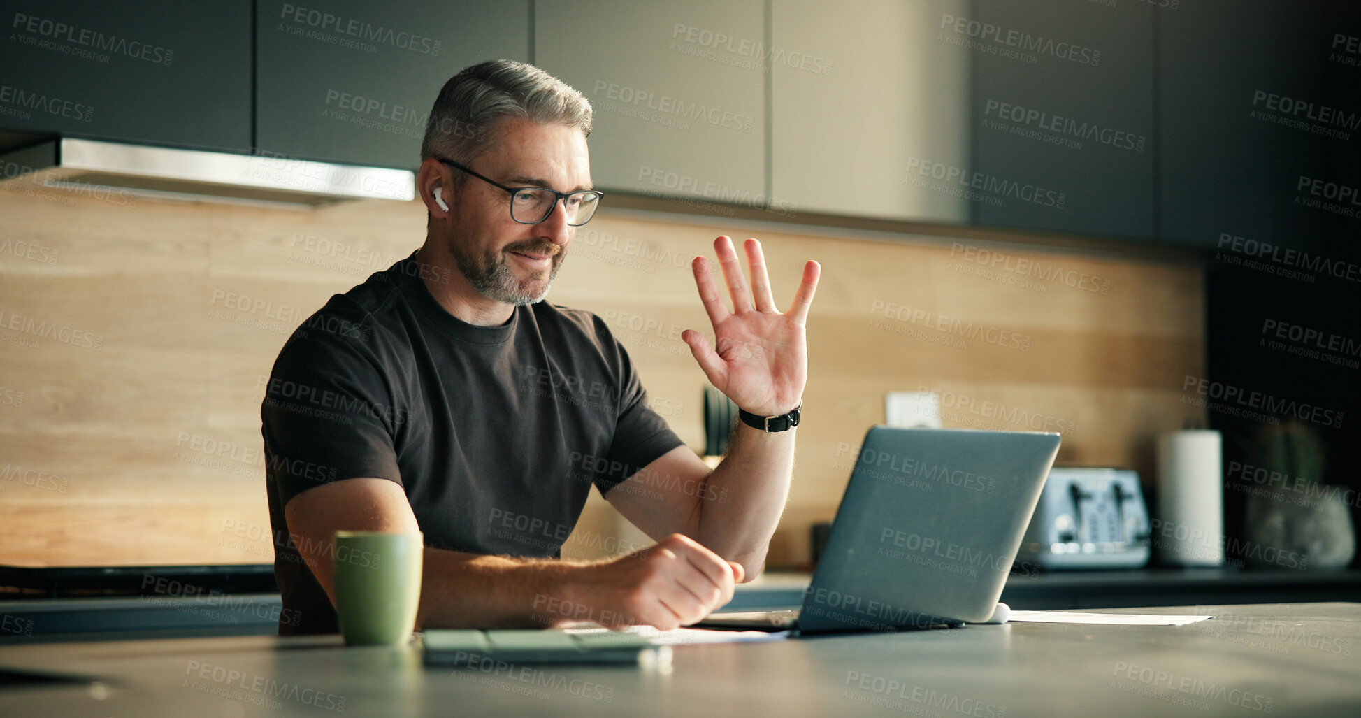 Buy stock photo Laptop, remote work and video call with man in kitchen of home for planning, report or research. Computer, earphones and wave with mature freelancer in apartment for virtual meeting or webinar